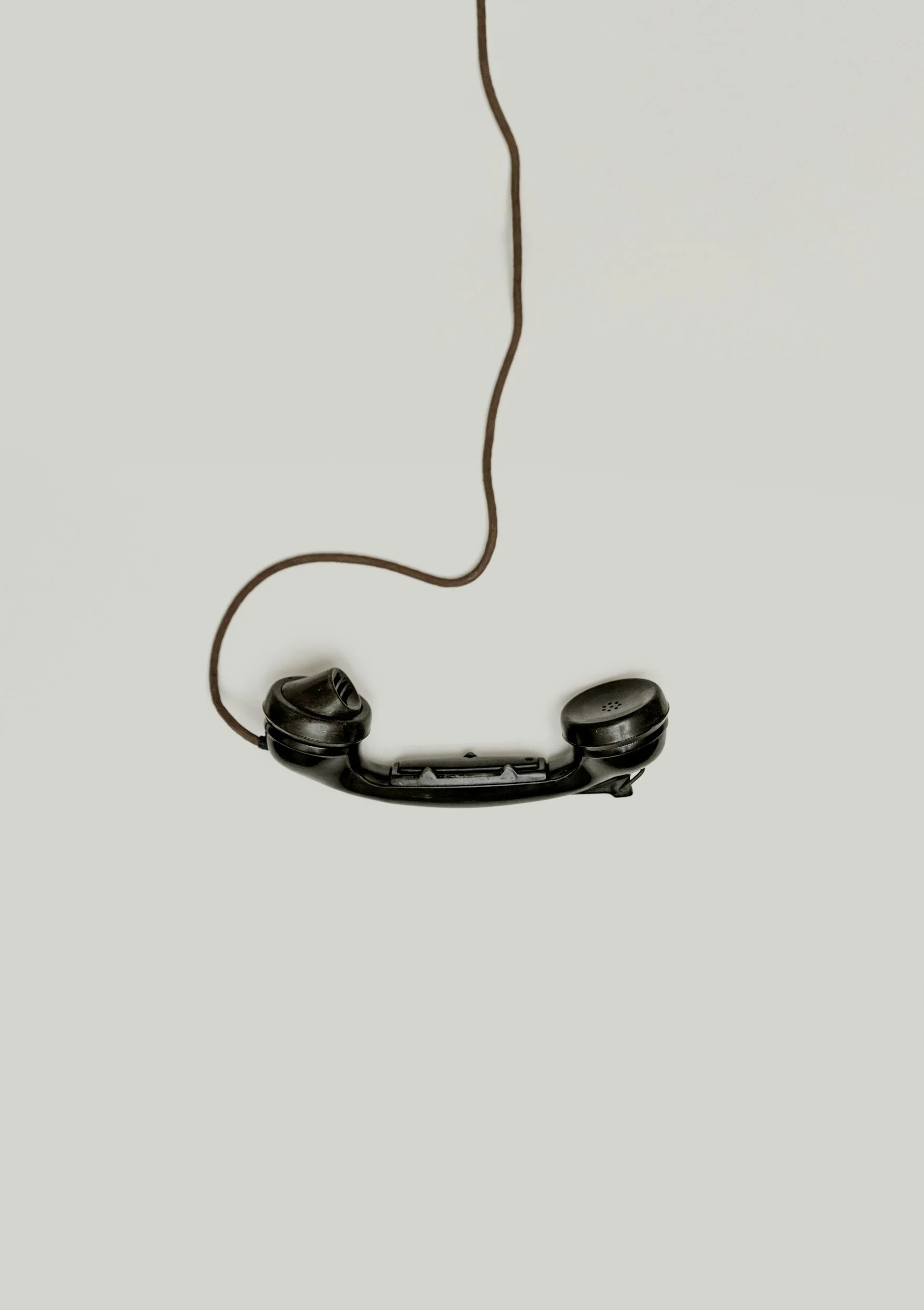 Vintage black telephone handset with cord on light gray background.